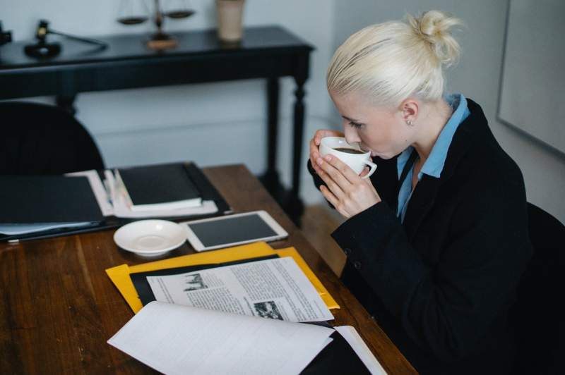 focused-young-female-lawyer-drinking-coffee-while-working-on-case-in-office
