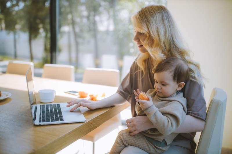woman-carrying-her-baby-and-working-on-a-laptop