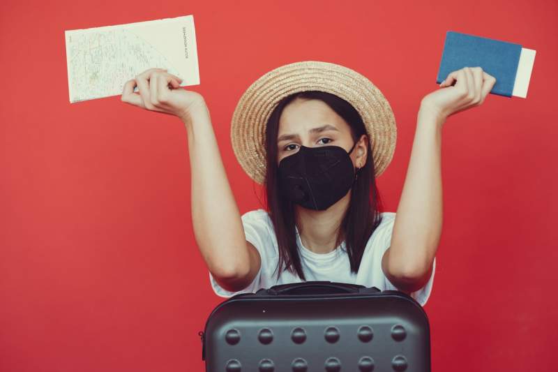 sad-woman-in-respiratory-mask-with-suitcase-and-passport